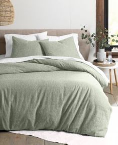 a bed with green sheets and pillows in a room next to a plant on the wall