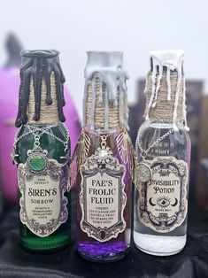 three bottles of liquid sitting next to each other on a black cloth covered tablecloth