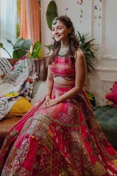 a woman in a red and gold bridal gown sitting on a couch next to a potted plant