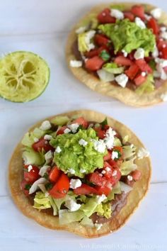 two tortillas topped with lettuce, tomatoes and avocado on a white surface