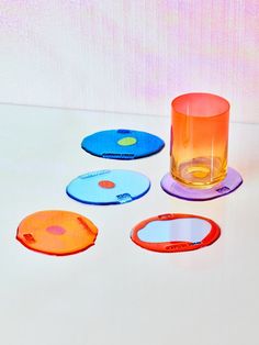 four different colored coasters sitting next to each other on a white counter top with a glass in the middle