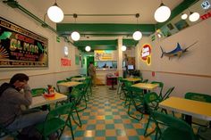 a woman sitting at a table in a restaurant with green chairs and yellow checkered floor