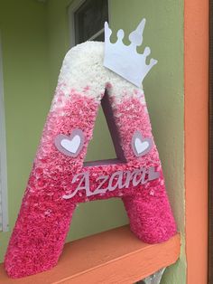 a pink and white letter with a crown on top is sitting on a shelf in front of a green wall