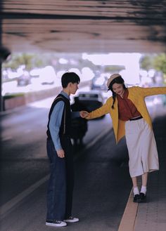 two people standing on the side of a road with their arms outstretched to each other