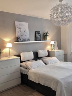 a white bed sitting in a bedroom under a chandelier next to a window