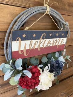 a welcome sign hanging on the side of a wooden wall with flowers in front of it