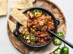 a bowl of chili and tortilla chips on a wooden plate with green peppers