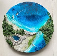 a blue plate with boats floating in the water and trees around it on a white surface