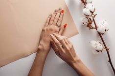 two hands holding each other over a piece of paper next to cotton flowers and branches