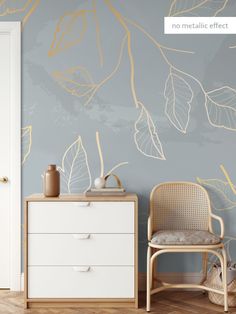 a white dresser sitting next to a chair in a room with blue walls and gold leaves on the wall