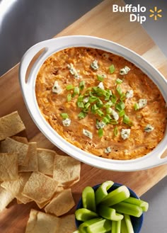 a bowl of dip next to chips and celery on a wooden cutting board