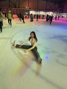 a woman is sitting on the ice at an indoor skating rink while others are walking around