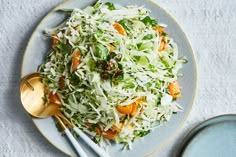 a white plate topped with shredded carrots and coleslaw next to two gold spoons