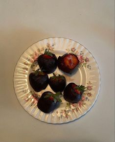 four strawberries on a plate with pink flowers and green leaves in the center, ready to be eaten