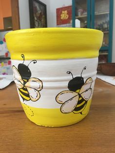 a yellow and white flower pot sitting on top of a wooden table with bees painted on it