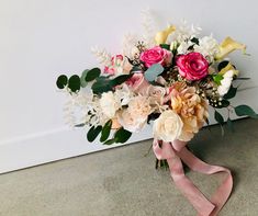 a bouquet of flowers sitting on the floor next to a white wall and pink ribbon