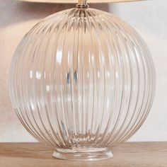 a clear glass table lamp sitting on top of a wooden table next to a white wall