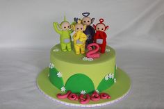 there is a green cake with pink decorations on the top and three small figurines atop it