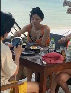 two women sitting at a table with food in front of them and one woman using her cell phone