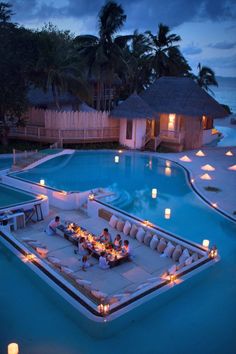 an outdoor dining area next to a swimming pool at night with candles on the tables