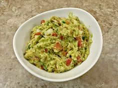 a white bowl filled with guacamole sitting on top of a marble counter