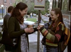 two women standing next to each other near a street sign with coffee cups in their hands