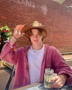 a young man wearing a hat sitting at a table with a drink in front of him