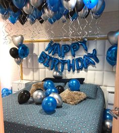 a bed with blue and silver balloons on top of it, next to a sign that says happy birthday