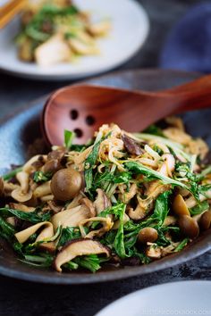 mushrooms and spinach stir fry in a bowl with a wooden spoon on the side