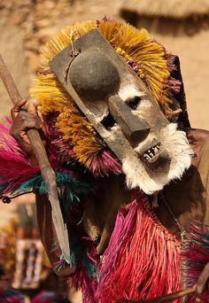 a man in an elaborate mask and feathered headdress holding a wooden stick