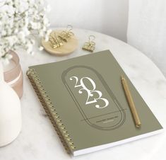 a spiral bound notebook sitting on top of a table next to a vase with flowers