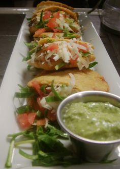 a white plate topped with three tacos and a bowl of guacamole