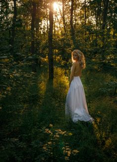 a woman in a white dress is walking through the woods with her back to the camera