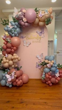 balloons and flowers are arranged on the floor in front of a wall with a sign that says little butterfly is one