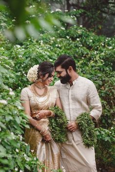 a man and woman standing next to each other in front of some bushes with greenery