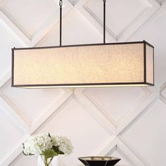 a lamp hanging over a table next to a vase with white flowers in it and a black bowl on the table