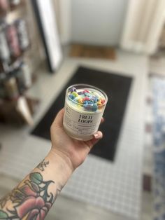 a person holding up an ice cream container with candy in it's hand on the floor