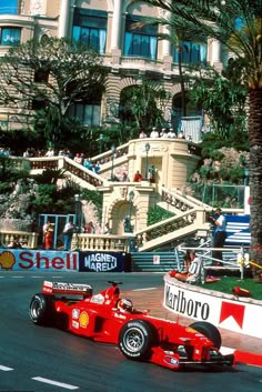 a man driving a red race car down a street in front of a tall building