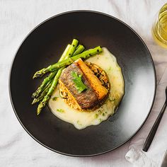 a black plate topped with meat and asparagus next to a glass of wine