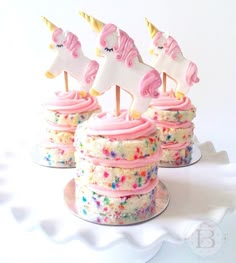 three cupcakes with pink frosting and unicorn decorations