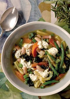 a white bowl filled with pasta and veggies on top of a floral table cloth