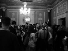 a group of people standing in a room with chandelier and paintings on the walls