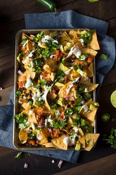 a tray filled with nachos sitting on top of a wooden table next to lime wedges