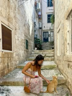 a woman kneeling down petting a dog in an alleyway with stone steps leading up to the door