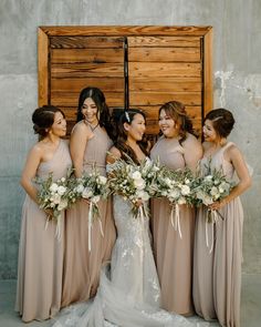 a group of women standing next to each other in front of a wooden door holding bouquets