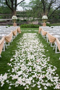 the aisle is lined with white chairs and rose petals