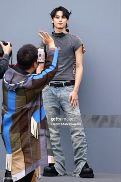 a man taking a photo with his cell phone while standing next to a woman in front of a gray wall