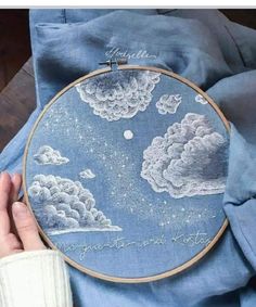 someone is holding up a embroidery project with clouds in the sky and stars on it