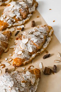 several pastries with almonds and powdered sugar on top sit on a piece of parchment paper