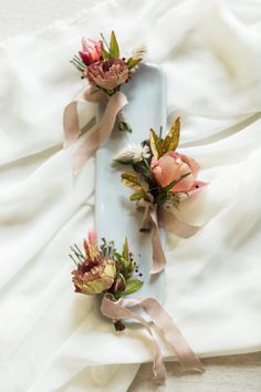 three flowers are placed on top of a blue tray with white sheets and pink ribbons